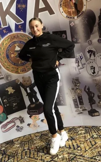 A Slater Stars dancer in team tracksuit beside the school's trophy display